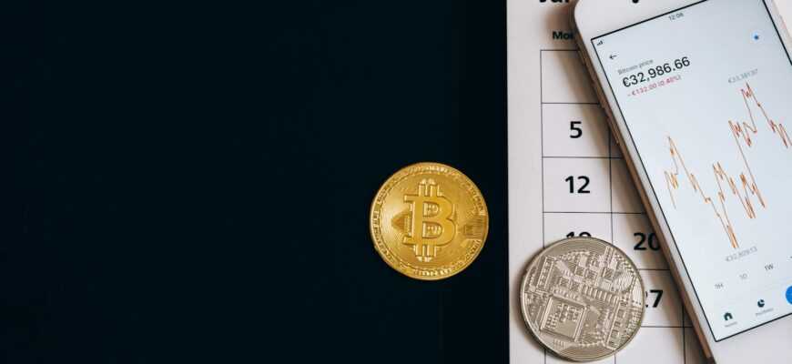 Bitcoin coins on a calendar with a smartphone showing price trends, illustrating finance dynamics.